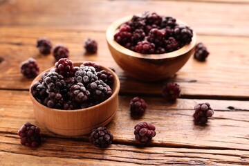 Ripe frozen blackberries in bowls on wooden table, closeup