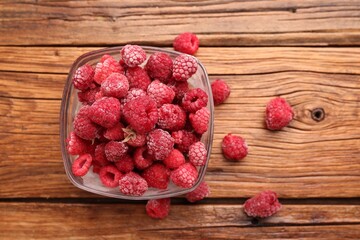 Ripe frozen raspberries in bowl on wooden table, flat lay