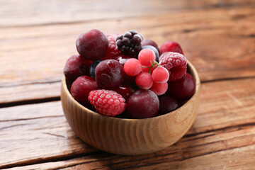 Mix of ripe frozen berries in bowl on wooden table, closeup