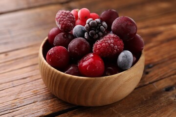 Mix of ripe frozen berries in bowl on wooden table, closeup