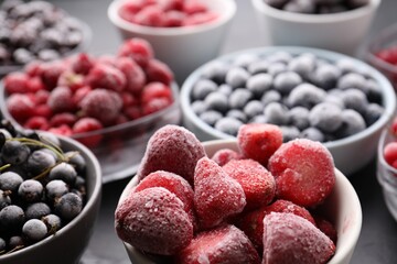 Different ripe frozen berries in bowls on grey table, closeup