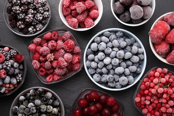 Different ripe frozen berries in bowls on dark textured table, flat lay