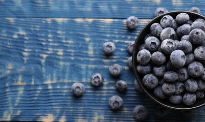 Ripe frozen blueberries in bowl on blue wooden table, flat lay. Space for text