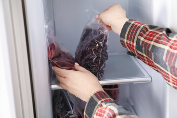 Woman taking plastic bags with frozen berries out of fridge, closeup