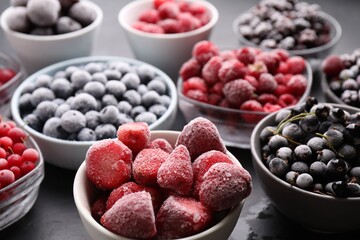 Different ripe frozen berries in bowls on grey table, closeup