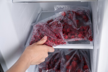Woman taking plastic bag with frozen red currants out of fridge, closeup