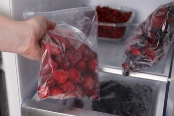 Woman with plastic bag of frozen strawberries near open fridge, closeup