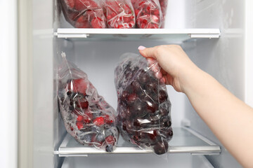 Woman taking plastic bag with frozen cherries out of fridge, closeup