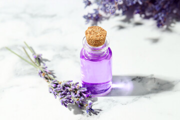 Aromatic essential oil in bottle and lavender flowers on white marble table, closeup