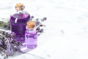 Aromatic essential oil in bottles and lavender flowers on white marble table, closeup. Space for...