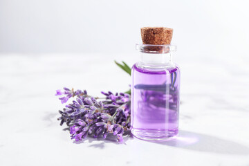Aromatic essential oil in bottle and lavender flowers on white marble table, closeup