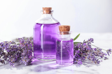Aromatic essential oil in bottles and lavender flowers on white marble table against light grey...