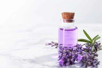 Aromatic essential oil in bottle and lavender flowers on white marble table, closeup. Space for text