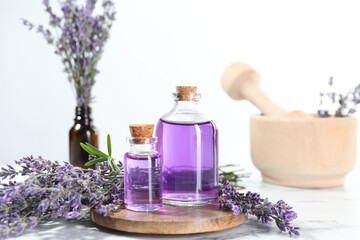Aromatic essential oil in bottles and lavender flowers on white marble table