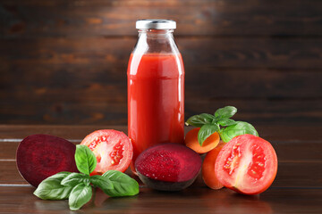 Tasty juice in glass bottle, fresh vegetables and basil on wooden table