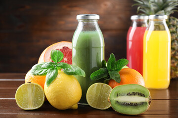 Tasty juices in glass bottles, fresh fruits, mint and basil on wooden table, closeup