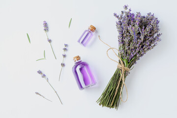 Aromatic essential oil in bottles and lavender flowers on white table, flat lay