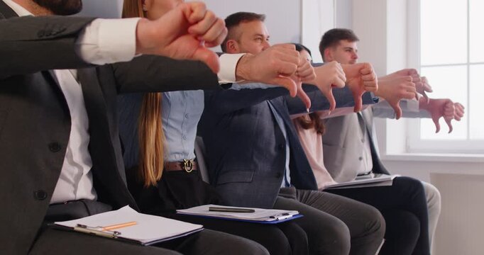 Displeased business people in a team show thumbs down to express dislike during an office meeting, focusing on group dissatisfaction in a professional setting with a sense of frustration.