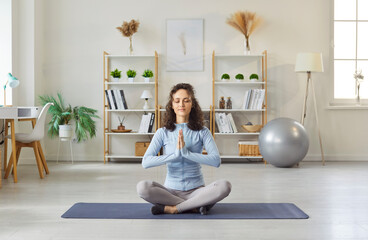 Portrait of a sporty peaceful woman wearing sportswear doing yoga exercise sitting on the floor in...