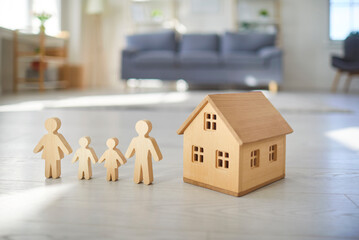 Wooden house miniature and figures of family stand in row on living room floor at home apartment....