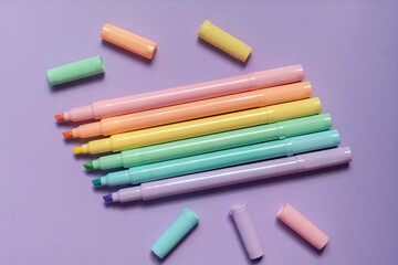 Flat lay of pastel color highlighters arranged neatly on purple background for creative school and office use.