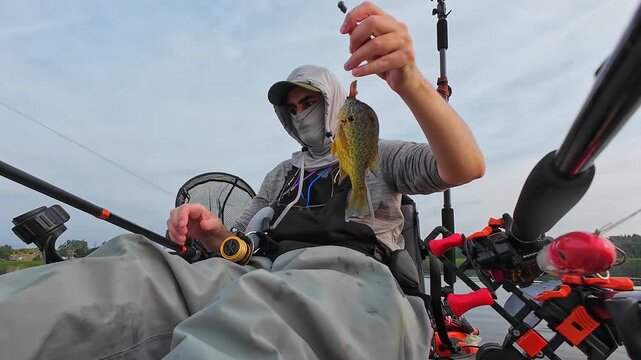 Angler in kayak catch and release nice panfish bluegill with hook and worm lure in its mouth, summer activity, kayaking and fishing outdoors. Kayak fisherman display his catch and release.