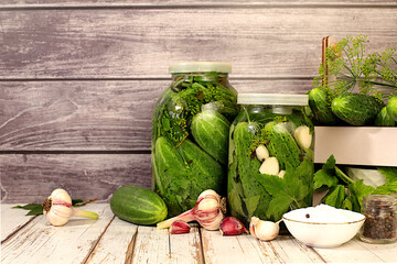 Pickled cucumbers in jars with garlic and dill on wooden kitchen table, rustic style,Homemade...