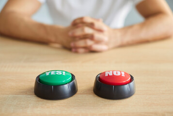 Closeup 2 buttons that read YES and NO on wooden table with man sitting in background, choosing to...