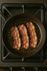  AI-generated image of three strips of bacon sizzling in a cast-iron pan on a stovetop, with hot oil bubbling for a classic breakfast scene.