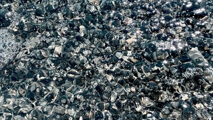 shimmering black pebble surface underwater with bright reflections and bubbles perfect for modern...