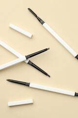 Automatic eyebrow pencils on beige background, flat lay