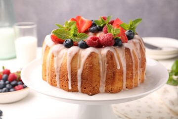 Delicious bundt cake with berries, glaze and mint on white table against grey background, closeup