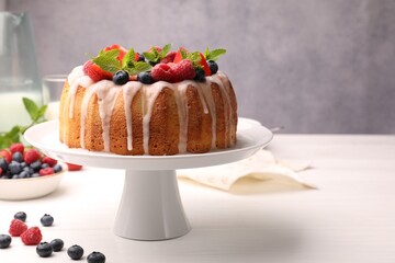 Delicious bundt cake with berries, glaze and mint on white wooden table against grey background, closeup