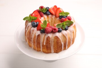 Delicious bundt cake with berries, glaze and mint on white wooden table, closeup