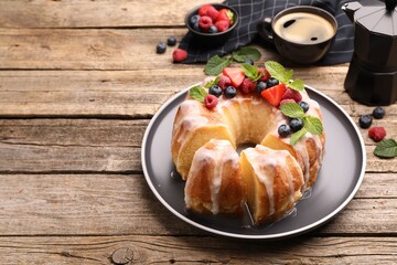 Pieces of delicious bundt cake with berries, glaze and mint on wooden table, closeup. Space for text