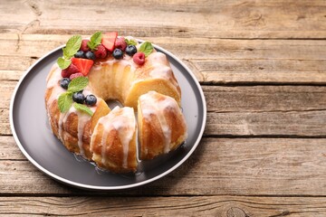 Pieces of delicious bundt cake with berries, glaze and mint on wooden table, closeup