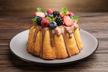 Tasty Bundt cake with berries, chocolate and mint on wooden table, closeup