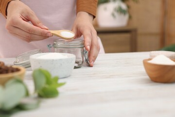Making natural scrub. Woman adding sugar into jar at white wooden table, closeup