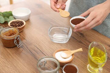 Making natural scrub. Woman adding coffee into bowl at wooden table, closeup