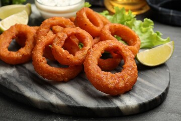 Fried squid rings, lime, lettuce and sauce on black table, closeup