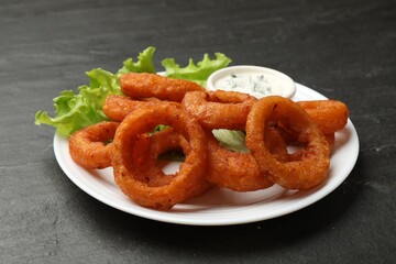 Fried squid rings served with sauce on black table, closeup