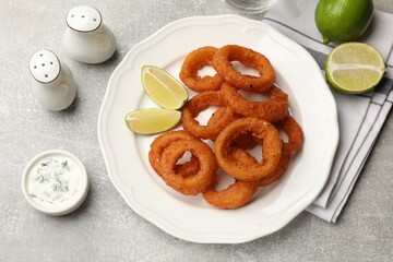 Fried squid rings, lime and sauce on grey table, flat lay