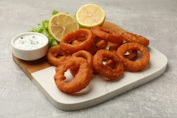 Fried squid rings, lemon, lettuce and sauce on grey table, closeup
