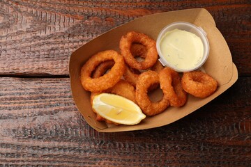 Fried squid rings, lemon and sauce on wooden table, top view. Space for text