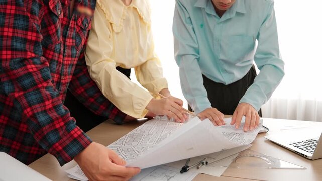 Professional engineer team discussion about house design on meeting table with architectural equipment and building blueprint scatter around at modern office. Focus on hand. Closeup. Delineation.