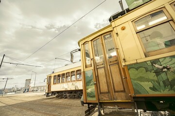 Two yellow vintage trams rest on cobblestone tracks in Porto, Portugal. The weathered paint and...