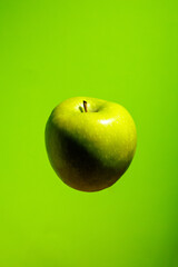 Whole green apple levitates on green background, representing natural farming, organic superfood, sports nutrition, vitamins, and healthy lifestyle