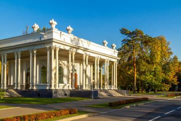 Pavilion with Stalinist architecture and oriental motifs at VDNH Exhibition Center, surrounded by autumn trees with yellow foliage and pines under blue sky. Moscow, Russia.