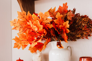 Bright autumn foliage arranged in a white vase on a rustic shelf in a cozy interior