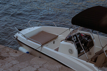 A detailed view of a small motorboat docked by a stone shore, with calm blue water creating a...